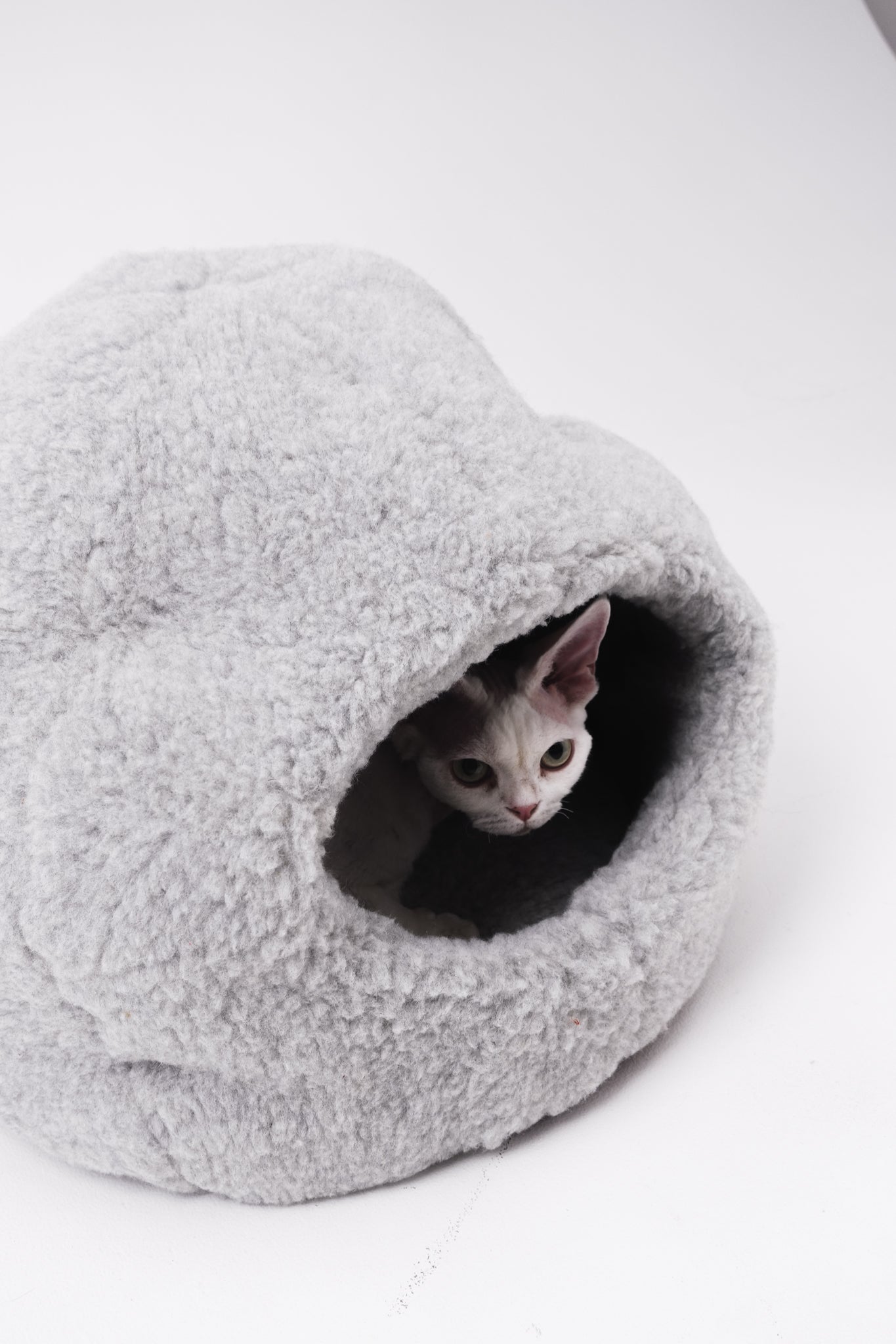 Cat peeking out from a gray fleece pet cave on a white background  | Natural, non‑toxic pet nest for cats and small dogs | Cozy, handmade pet furniture
