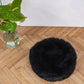 An Round Natural Sheepskin Pet Bed - Black on a wooden floor.
