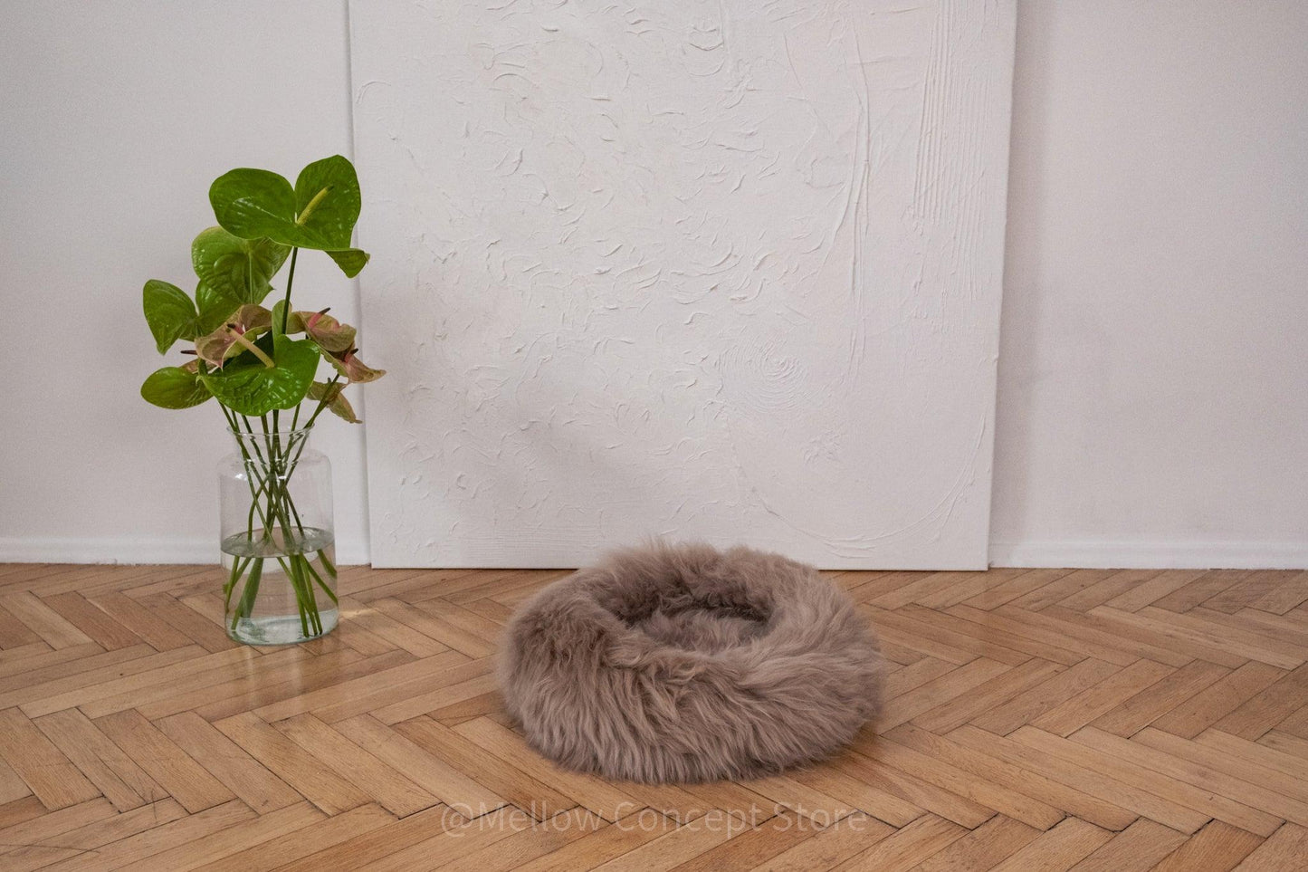 A Round Natural Sheepskin Pet Bed in Greige from Mellow Pet Store on a wooden floor made from sustainable materials.