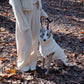 A woman with a Mellow Pet Store woolen dog vest in white standing in the woods, enjoying the natural surroundings.