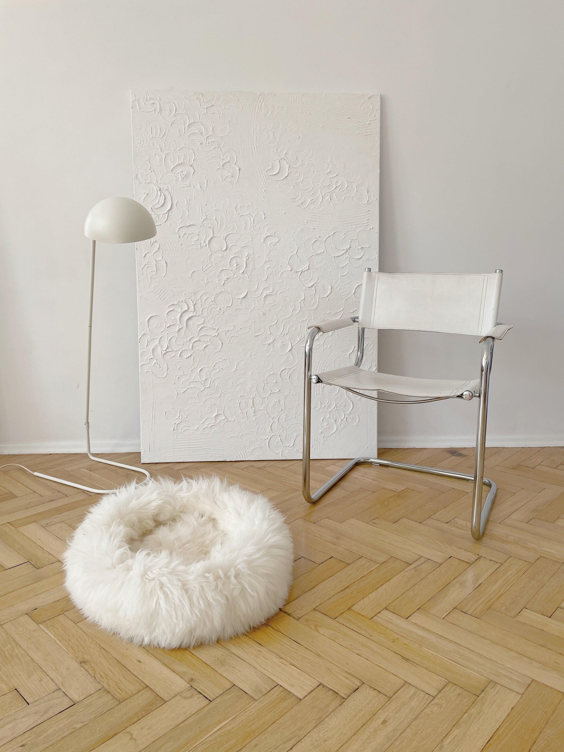 A Round Natural Sheepskin Pet Bed from Mellow Pet Store is resting on a wooden floor.